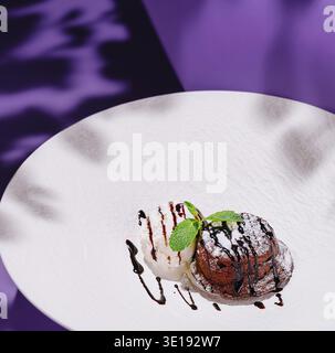 Dessert fondant au chocolat avec glace à la vanille décorée de feuilles de menthe et sauce au chocolat sur plaque blanche sur fond violet avec des ombres Banque D'Images