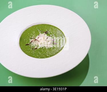 La soupe à la crème verte est servie dans une assiette blanche sur fond vert, garnie de parmesan et de microverts Banque D'Images