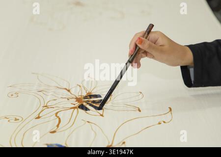 Gros plan main de femme avec pinceau peinture Batik sur tissu de batik malaisien Banque D'Images