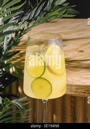 Grand verre de cocktail d'été rafraîchissant est debout sur une table en bois avec des plantes tropicales en arrière-plan Banque D'Images