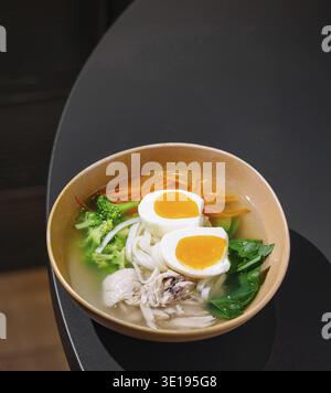 Soupe salée de nouilles au poulet avec légumes et œufs servie dans un cadre moderne de restaurant Banque D'Images
