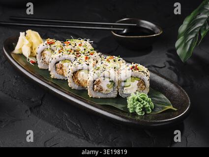 Rouleaux de sushi au saumon et au fromage à la crème recouverts de graines de sésame couchés sur une assiette noire sur une table en pierre sombre Banque D'Images
