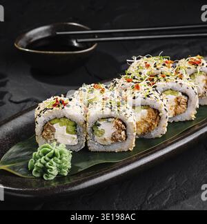 Rouleaux de sushi au saumon et au fromage à la crème recouverts de graines de sésame couchés sur une assiette noire sur une table en pierre sombre Banque D'Images