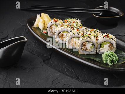 Rouleaux de sushi au saumon et au fromage à la crème recouverts de graines de sésame couchés sur une assiette noire sur une table en pierre sombre Banque D'Images