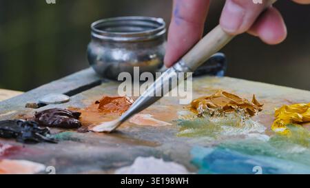 Peintre mélangeant des peintures à l'huile sur palette avec pinceau dans un studio d'art. Banque D'Images