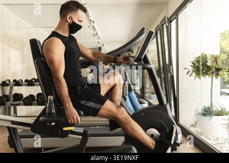 Jeune homme sportif portant un masque de prévention pendant son entraînement en salle de gym Banque D'Images