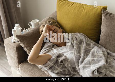 Femme malade qui coute la couverture et qui souffre de maux de tête à la maison Banque D'Images