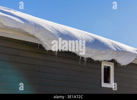 Glaçons d'hiver suspendus à un toit couvert par la neige d'une maison en bois Banque D'Images