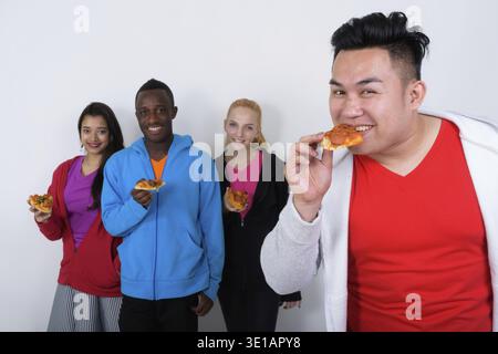 Happy Young Asian man eating Tranche de pizza avec divers groupes de multi ethnic friends smiling and holding Tranche de pizza ensemble Banque D'Images