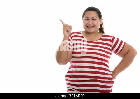 Studio shot of young happy fat woman smiling while pointing finger up Banque D'Images