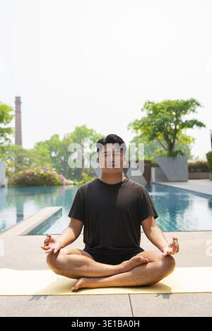 Jeune homme asiatique faisant de l'exercice de yoga à côté de la piscine pendant l'été Banque D'Images