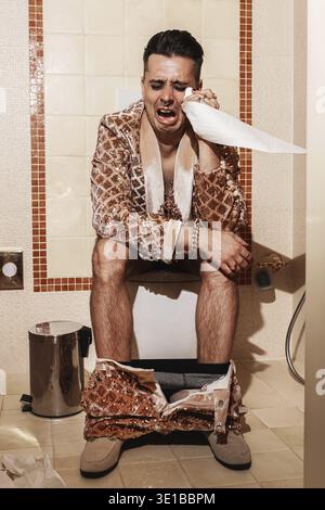 Homme riche, vêtu d'un costume doré radieux, assis sur une toilette et pleure Banque D'Images
