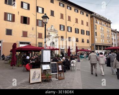 Piazza della Vettovaglia. Tables de restaurant sous des parasols rouges sur la place européenne. Les gens dînent et marchent à Pise Italie. Banque D'Images