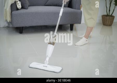 Belle femme asiatique nettoyant le salon dans la maison balayant le sol à l'aide d'un tampon de serpillère humide en microfibre. routine de nettoyage des devoirs. Entretien domestique Banque D'Images