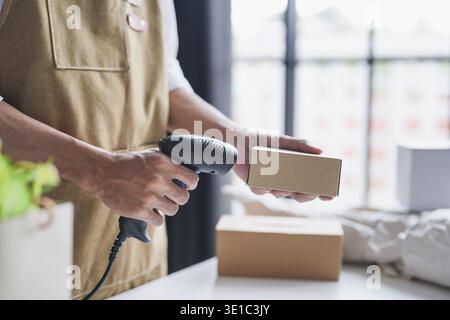 Propriétaire de petite entreprise asiatique utilisant un lecteur de codes-barres portable pour vérifier et gérer les stocks de produits dans un magasin de détail local pendant les opérations de l'après-midi Banque D'Images