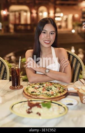 Portrait d'une belle jeune femme asiatique avec de longs cheveux noirs dans la ville de style européen manger le dîner. Élégant touriste féminin en plein air, appréciant pittoresque Banque D'Images