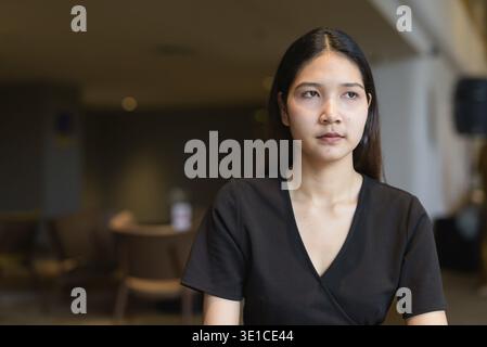 Jeune femme asiatique assise dans un café portant une robe noire élégante Banque D'Images