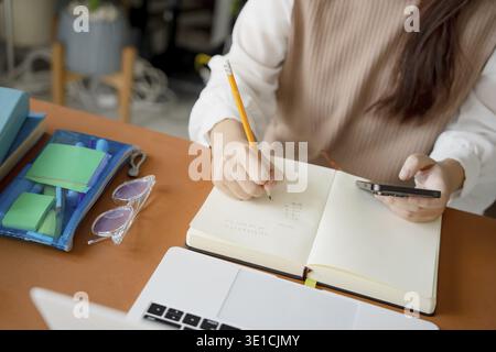 Étudiante asiatique faisant examen main tenant crayon écriture réponse dans l'enseignement en classe universitaire lycée ou étudiant universitaire prenant des notes whil Banque D'Images