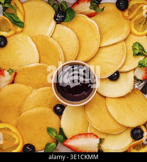 Un plateau vibrant présente une variété de crêpes dorées disposées magnifiquement avec des tranches de fraises, de myrtilles, de citron et de menthe Banque D'Images