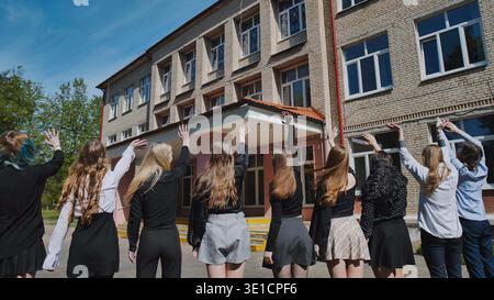 Groupe d'étudiants heureux saluant l'école le dernier jour, célébrant la fin de l'année scolaire Banque D'Images
