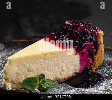 Tranche de cheesecake crémeux garnie d'une compote de baies vibrante et de sucre en poudre, élégamment servie sur une assiette sombre Banque D'Images