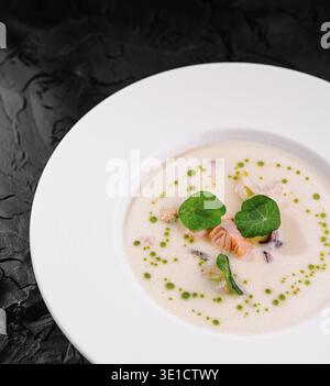 Soupe de fruits de mer luxueuse avec des herbes fraîches présentée habilement sur une assiette blanche avec un fond texturé noir Banque D'Images