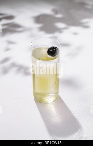 Un grand verre de gin tonic projette des ombres sur une table blanche sous le soleil d'été Banque D'Images