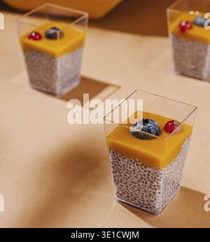 Trois desserts chia pudding avec purée de mangue garnie de baies, élégamment présentés Banque D'Images