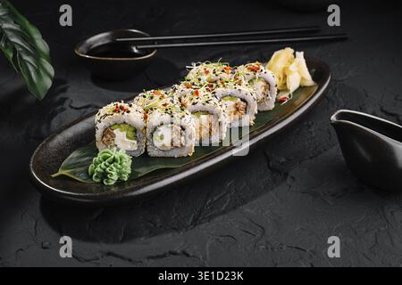 Rouleaux de sushi au saumon et au fromage à la crème recouverts de graines de sésame couchés sur une assiette noire sur une table en pierre sombre Banque D'Images