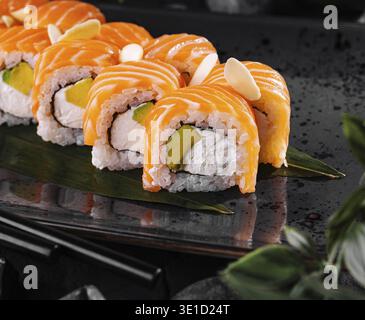 Des rouleaux de sushi au saumon, à l'avocat, au fromage à la crème et au concombre sont servis sur une assiette noire Banque D'Images