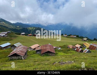 Pittoresque village de montagne avec des cabanes traditionnelles en bois avec des toits rustiques dispersés dans des prairies verdoyantes. Pics nuageux spectaculaires et salut boisé Banque D'Images