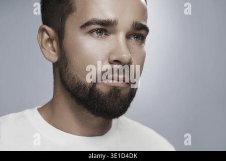 Portrait de jeune et beau homme barbu avec la peau propre sur fond gris Banque D'Images