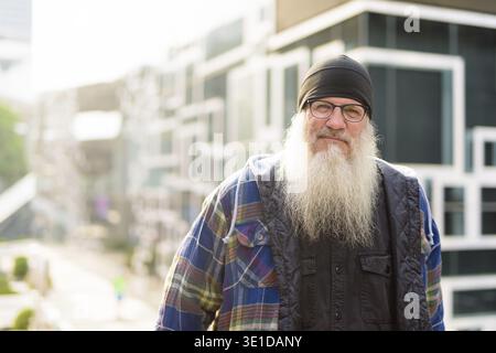 Portrait d'homme hipster mûr beau barbu contre le mur avec un design abstrait dans les rues de la ville à l'extérieur Banque D'Images