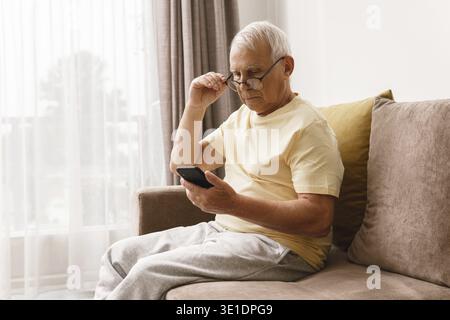 Un homme âgé portant des lunettes utilise un smartphone à la maison Banque D'Images