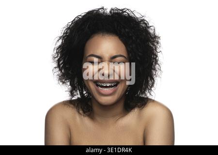 Heureuse femme noire souriante avec des bretelles dentaires sur ses dents sur fond blanc Banque D'Images