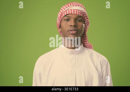 Studio shot of young African man wearing vêtements musulmans traditionnels contre un arrière-plan vert Banque D'Images