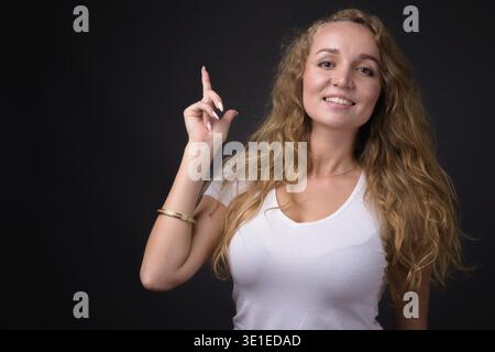 Photo studio de jeune belle femme avec long blond ondulé cheveux sur fond gris Banque D'Images