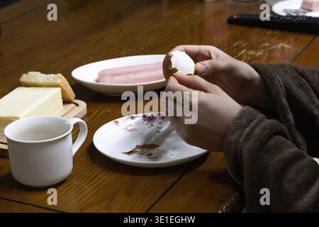 Femme épluchant l'œuf dur à la table du petit déjeuner, repas du matin sain à la maison Banque D'Images