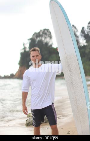 Mannequin occasionnel posé à côté de Surfboard par Ocean. Photographie de femme en T-shirt avec planche de surf à la plage Banque D'Images