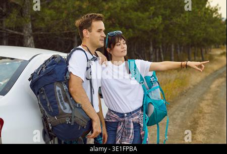 Couple avec des sacs à dos en voiture, pointant vers le sentier forestier sur la route rurale Banque D'Images