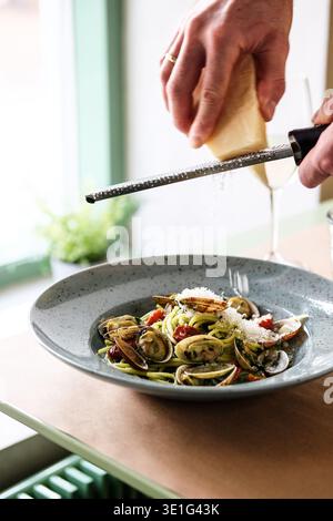 Cuisson préparation de fromage. Scène rustique où le chef râpe du fromage sur des pâtes aux moules à la lumière naturelle Banque D'Images