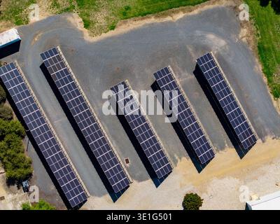 Une vue aérienne capte cinq rangées parallèles de panneaux solaires photovoltaïques sombres installés sur une surface de gravier de couleur claire, bordée de l vert Banque D'Images