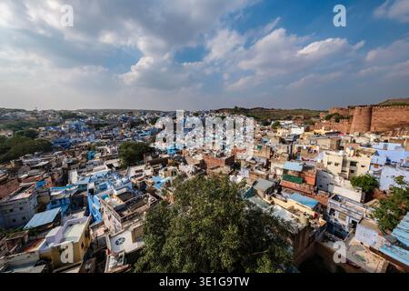 Les maisons densément remplies de la vieille ville de Jodhpur mènent vers l'imposant fort de Mehrangarh sur une colline rocheuse sous un ciel lumineux avec des nuages éparpillés. Banque D'Images