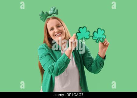Rousse jeune femme avec décor en forme de trèfle sur fond vert. Célébration de la fête de Patrick Banque D'Images