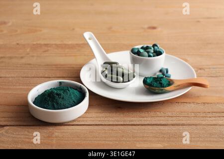 Bols de poudre de spiruline avec comprimés et capsules sur fond en bois Banque D'Images