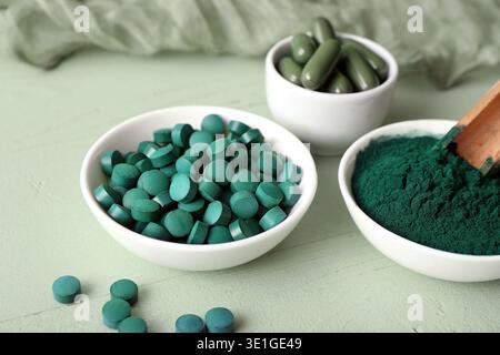 Bols de poudre de spiruline avec des capsules et des comprimés sur fond de bois vert Banque D'Images