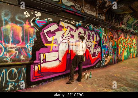 Un artiste graffiti au travail dans Leake Street Graffiti tunnel, célèbre espace d'art urbain situé sous la gare de Waterloo à Londres Banque D'Images