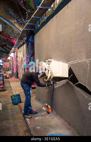 Un artiste graffiti au travail dans Leake Street Graffiti tunnel, célèbre espace d'art urbain situé sous la gare de Waterloo à Londres Banque D'Images