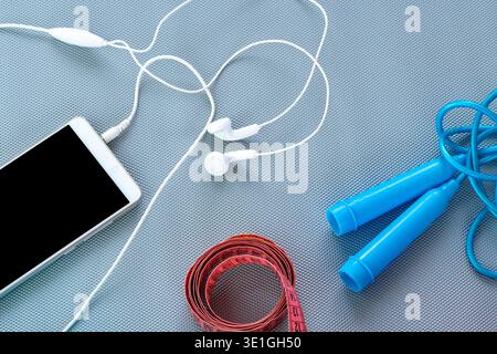 Une composition à plat comprenant un smartphone, des écouteurs, une poignée de corde à sauter et un ruban à mesurer sur fond gris. Concept de gestion du poids, Banque D'Images
