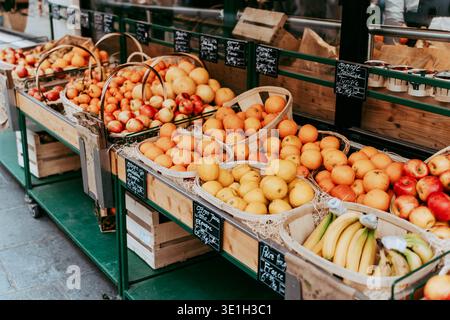 Fruits frais exposés à un étal coloré de marché de rue. Oranges, pommes et bananes disposées dans des caisses en bois créent une scène vibrante de produ local Banque D'Images